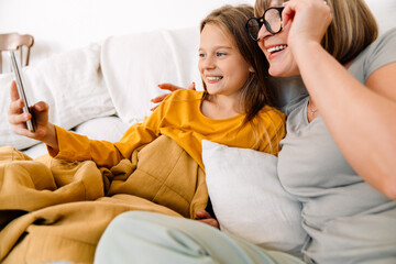 White girl and her grandmother using mobile phone while sitting on sofa