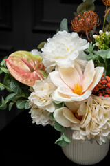 Plastic handmade bouquet artificial flowers composition.Beautiful flowers in vase on a table with black  background. Women's, mother's day. Spring, summer season. Front view.Selective focus.
