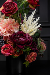 Plastic handmade bouquet artificial flowers composition.Beautiful flowers in vase on a table with black  background. Women's, mother's day. Spring, summer season. Front view.Selective focus.
