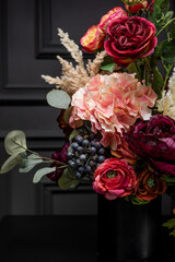 Plastic handmade bouquet artificial flowers composition.Beautiful flowers in vase on a table with black  background. Women's, mother's day. Spring, summer season. Front view.Selective focus.
