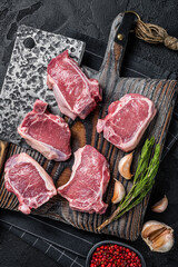 Fresh Raw lamb loin chops steaks, cutlets on butcher board with meat cleaver. Black background. Top...