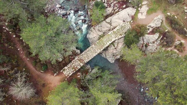 Birds-eye view pulling back above an ancient Genoese bridge over the clear water of the fast flowing Tartagine river in the Balagne region of Corsica