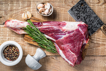 Fresh Raw lamb or goat leg with rosemary and pepper on cutting board. wooden background. Top view