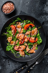 Salmon salad with fish slices, arugula, tomato and green vegetables. Black background. Top View