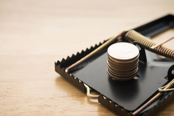 Stacked coins in a rat trap on wooden background. Online internet financial scam, internet fraud, fishing hacker, risk investment concept.