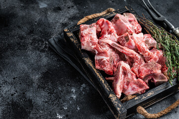 Raw diced meat with bone in a wooden tray. Black background. Top View. Copy space