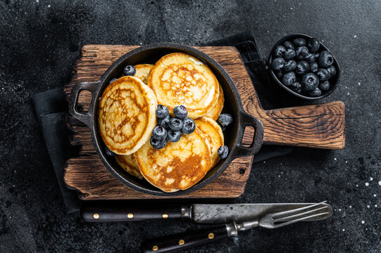 Pancakes with fresh blueberries and maple syrup in a pan. Black background. Top View