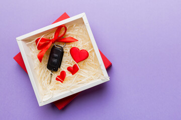 Black car key in a present box with a ribbon and red heart on colored background. Valentine day composition Top view