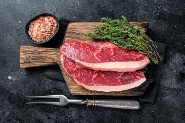 Uncooked Raw rump steak or top sirloin cap beef meat steaks on wooden board. Black background. Top view