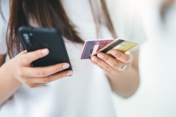 Focus on hand young asian woman holding mock up of credit cards and using mobile phone to shopping or paying online