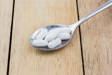 Oral medicine pills on spoon, paracetamol on spoon, white pills on wooden table, wood background