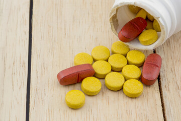 Red and yellow medicine pills spilled out of bottle on wooden table, wood background.