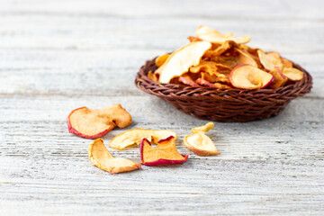 A pile of dried slices of apples in wicker basket on white wooden background. Dried fruit chips. Healthy food