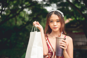 An attractive young asian woman with a shopping bag and sipping on iced coffee. Outdoor al fresco...
