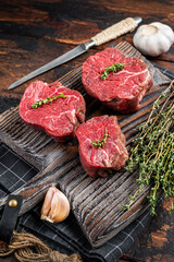 Prime raw Fillet mignon steaks on a wooden board with thyme and garlic. Dark wooden background. Top view