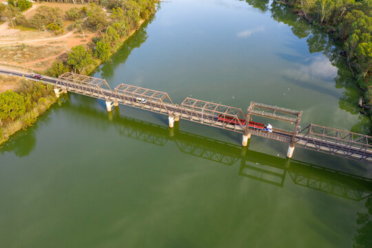 Aerial view of a truck crossing a metal span bridge over a wide green river