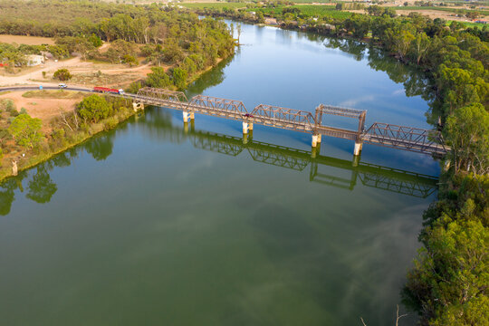 Aerial view of a truck approaching a metal span bridge over a wide green river