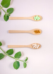 healthy food supplements in capsules: chlorella, fish oil, psyllium and mint sprigs on a light background