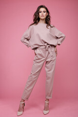 High fashion photo of a beautiful elegant young woman in a pretty pink jumpsuit posing on pink background. Slim figure. Studio Shot. Luxurious hair, shiny curls. Femininity and tenderness. Monochrome