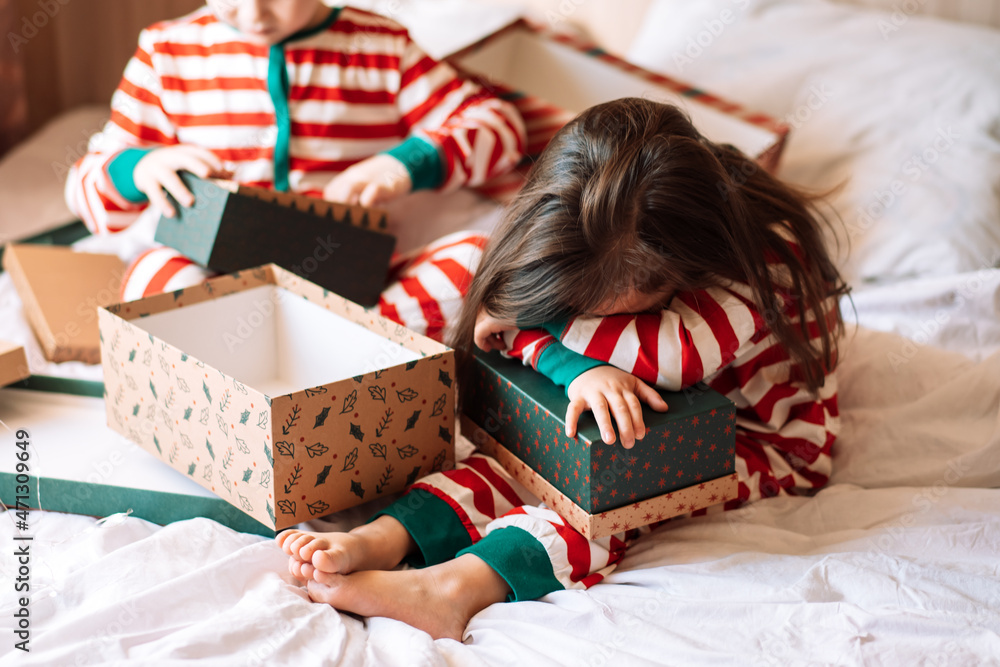 Wall mural siblings in pajamas unpack christmas gifts while sitting on white bed