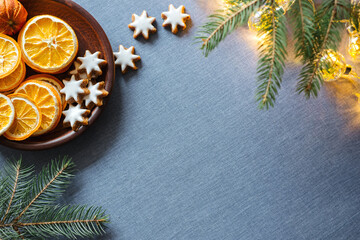 Fototapeta na wymiar Winter background with dried oranges, ginger cookies pine tree branch and shiny garland on blue tablecloths. Top view, copy space