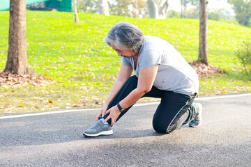 Asian elderly woman jogging in the park in the morning She had an ankle injury from exercising. She felt a lot of pain. concept of health care for seniors to be healthy - obrazy, fototapety, plakaty
