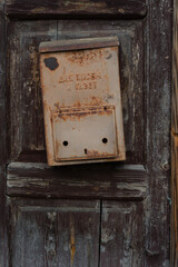 Attached to the wooden door with remnants of dark peeling paint is an old, vintage and rusty metal mailbox with remnants of yellow paint.