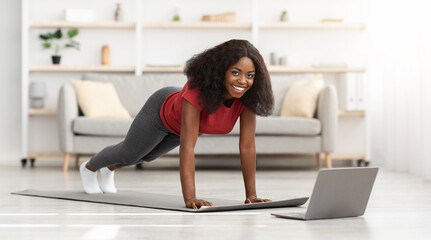Positive african american athletic woman exercising at home, using laptop