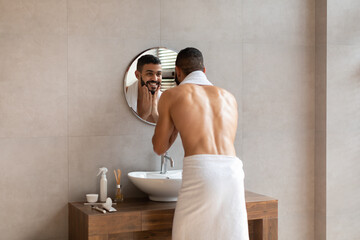 Confident young guy looking in the mirror, touching beard