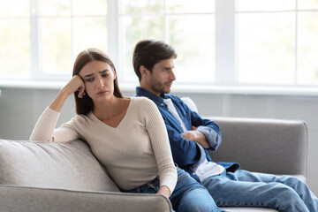 Obraz premium Sad depressed young caucasian wife ignores unhappy husband sitting on sofa in living room interior