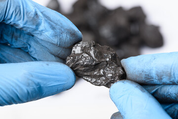 Hands in gloves hold lump of black coal in laboratory. Fossil fuel research concept.