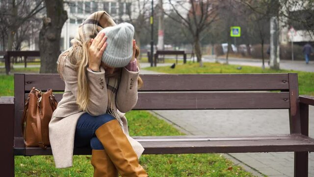 Young woman sitting on a park bench in a depressed and bad mood.