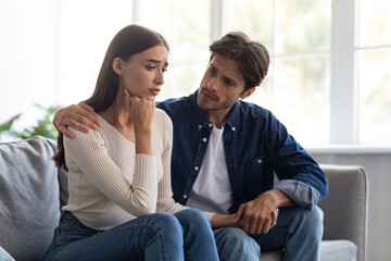 Careful european millennial man calms unhappy sad offended woman after quarrel in living room interior