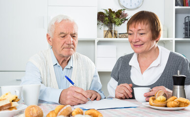 Elderly couple studying agreement conditions before signing at home