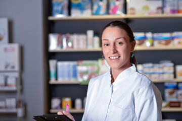 Young pharmacist standing next to medicine shelves, holding tablet