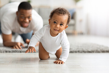 Cute Black Infant Baby Crawling At Home, Proud Father Looking At Him - obrazy, fototapety, plakaty
