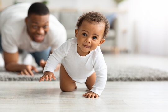 Cute Black Infant Baby Crawling At Home, Proud Father Looking At Him