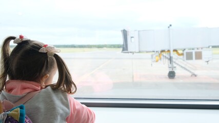 little girl aged 5 years looks out the window at the airport, waiting for the departure or arrival of the plane, dreaming of a trip