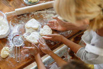 Cropped image of a female and kid hands holding dough in heart shape top view.