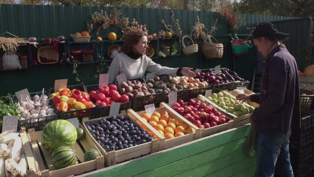 2 Shots. A man buys apples at the farmers' market. A woman seller gives him a plastic bag and he puts apples in it.  The customer pays in cash. Shooting in two cameras. 