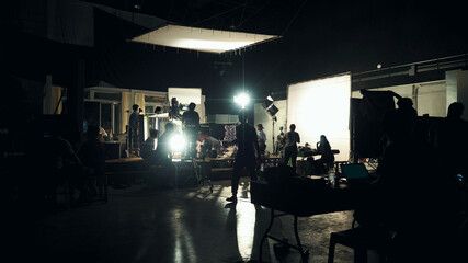 Video recording camera and lighting set up. Silhouette of film crew working in big production...
