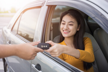 Young beautiful asian women buying new car. she very happy and excited. Sit in and getting car key. Smiling female driving vehicle on the road on a bright day