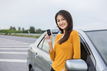 Young beautiful asian women buying new car. she was standing in near car on the roadside. Hand showing car key. Smiling female driving vehicle on the road on a bright day
