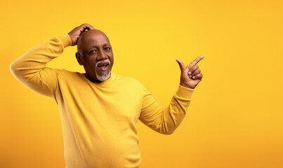 Shocked senior African American man pointing aside at empty space over orange studio background,...