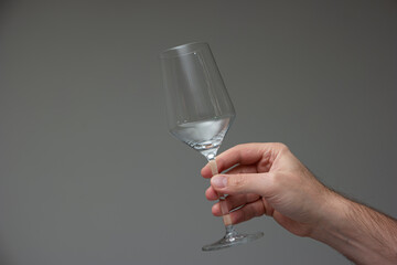 Empty wine glass held in hand by Caucasian male hand. Close up studio shot, isolated on gray...