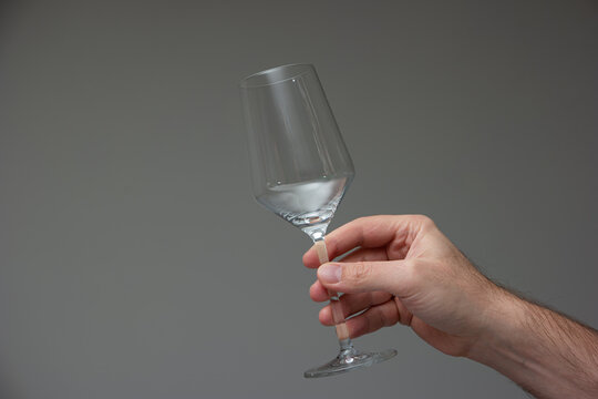 Empty wine glass held in hand by Caucasian male hand. Close up studio shot, isolated on gray background