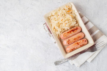 Top view of traditional dish is fried sausages and pickled cabbage salad in a red rectangular plate with fork on a napkin on light table