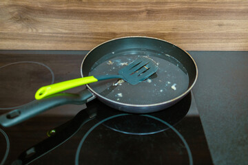 Dirty frying pan with plastic spatula on induction glass hob on modern kitchen