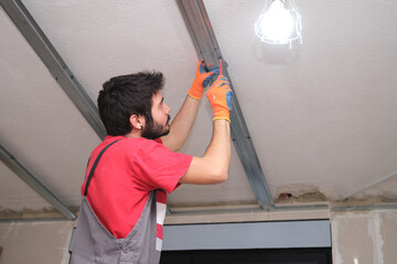 Worker assembling a suspended ceiling metal frame with a screwdriver.