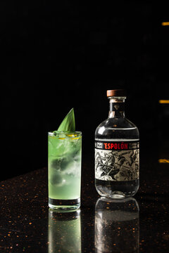 Minsk/Belarus - 11-24-2021: A light green alcoholic cocktail in a highball glass with ice, garnished with a bamboo leaf, at the bar counter, and a bottle of Tequila Espolon Blanco